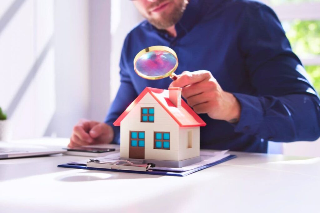 man looking down at a small home through a magnifying glass