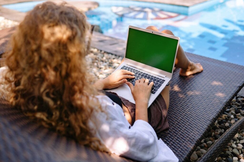woman sitting outside working on a laptop by the pool