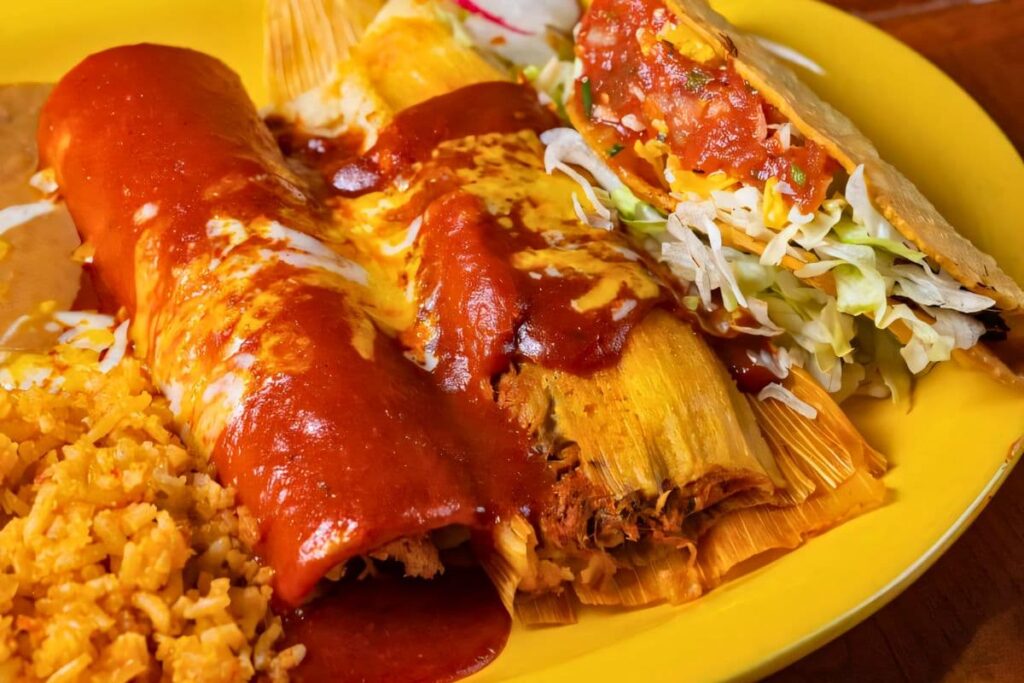 Enchilada, tamale, and hard shell taco served with Mexican rice and refried beans