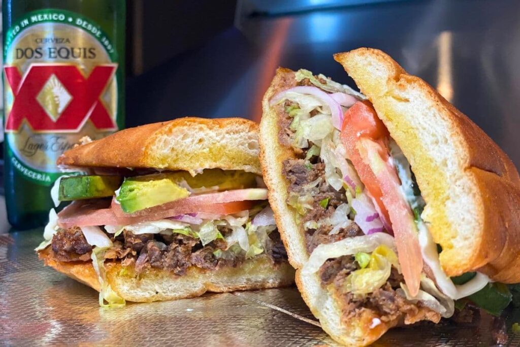 Mexican asada torta cut in half with a Dos Equis